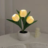 A cluster of glowing yellow LED tulips in a white ceramic pot used as a night light.