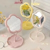 A set of three floral decorative desktop mirrors in yellow, pink, and white on a white surface.