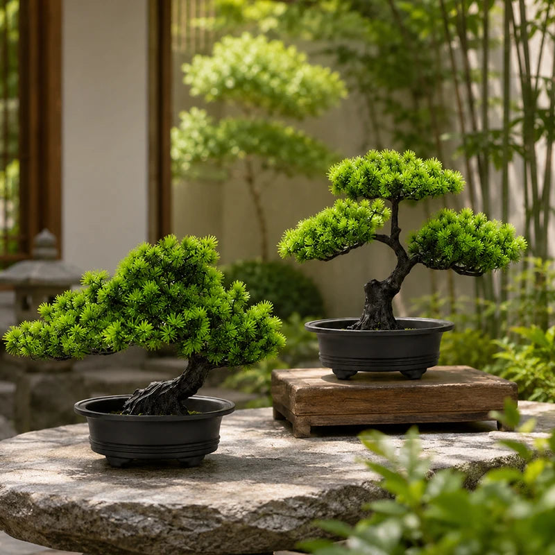 Artificial bonsai pine tree in a black pot displayed on a stone surface with lush green foliage in a garden setting