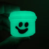 A glowing neon green miniature pumpkin bucket with a smiling face is held in a hand against a dark background.