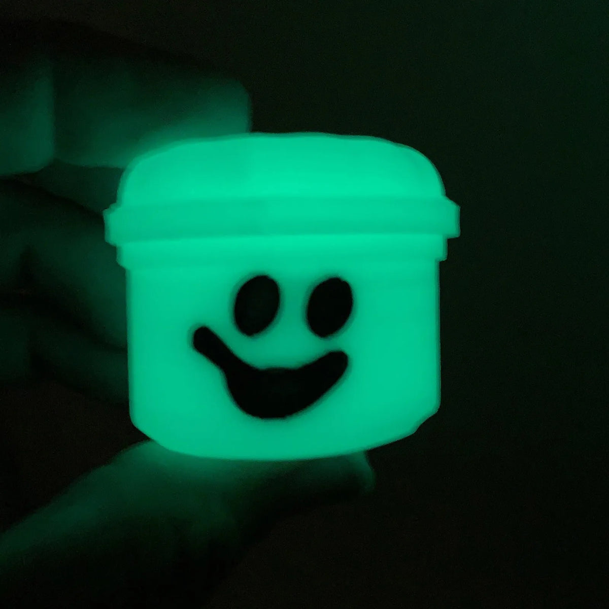 A glowing neon green miniature pumpkin bucket with a smiling face is held in a hand against a dark background.
