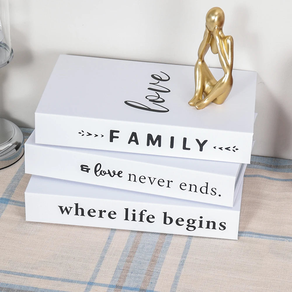 A set of three modern decorative fake books in white featuring gold accents and text about love, family, and life.