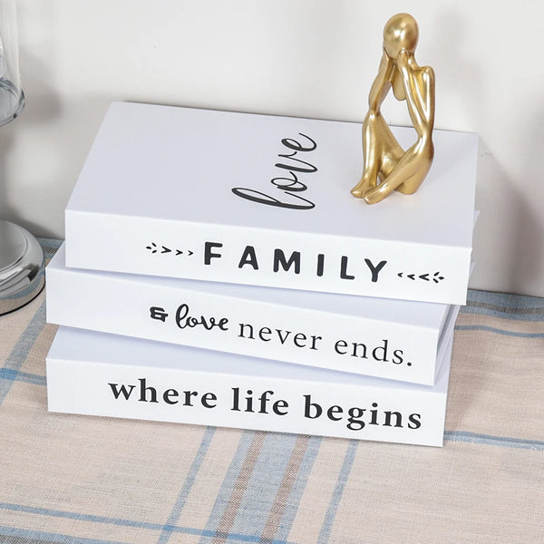 A set of three modern decorative fake books in white featuring gold accents and text about love, family, and life.