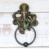 A bronze octopus skull door knocker featuring a cast iron ring on a white wooden surface.