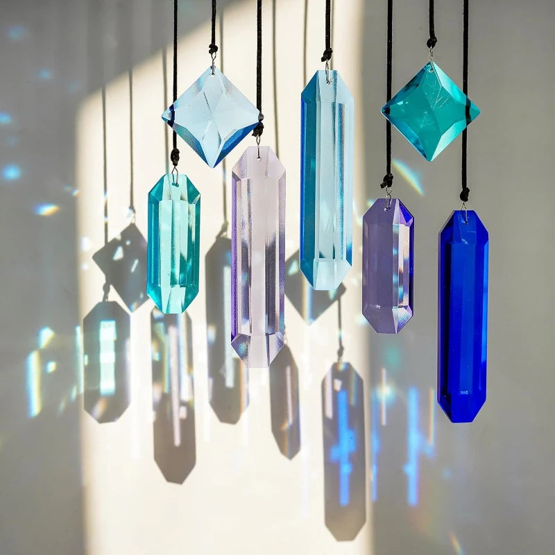 A collection of seven hanging crystal prism sun catchers in various shades of blue, purple, and teal casting colorful light p