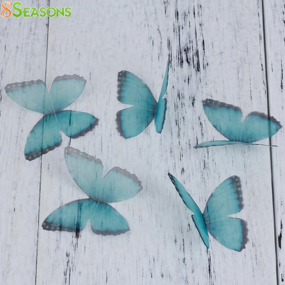 Light blue and gray organza butterfly embellishments scattered on a white wooden surface.