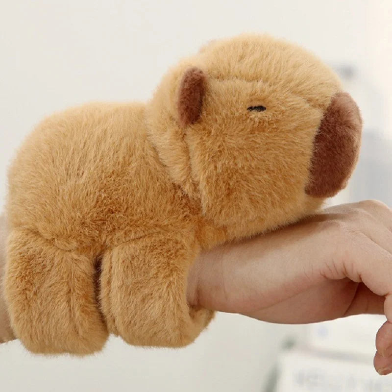 A small, light brown capybara animal wristband is being held by a person's hand.