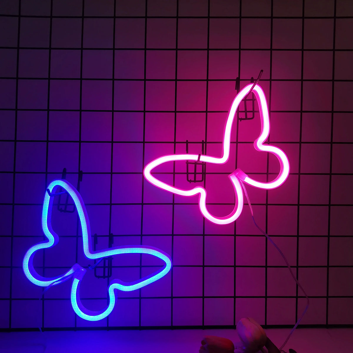 Two glowing neon butterfly signs, one pink and one blue, are displayed against a dark grid background.