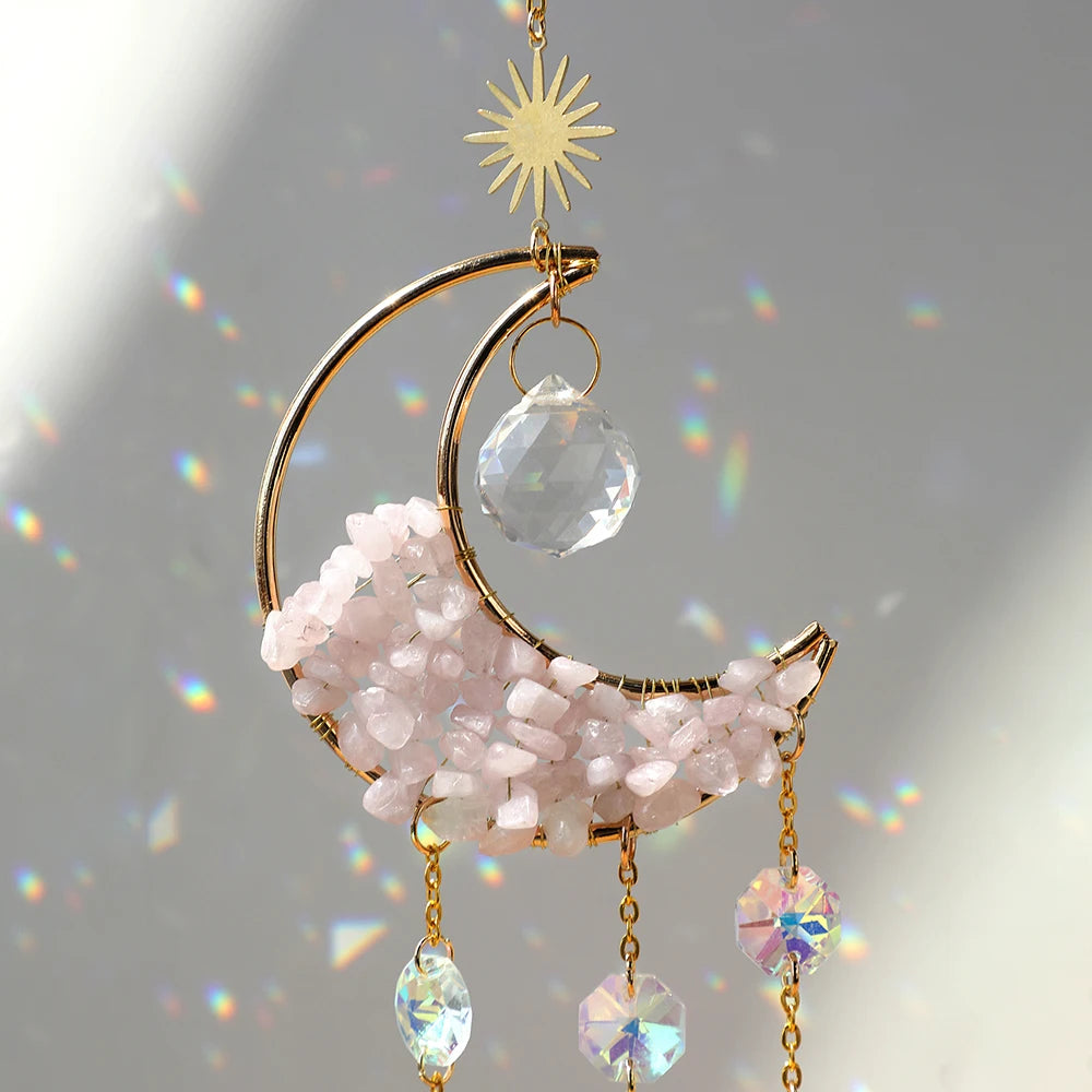 A gold moon-shaped crystal suncatcher featuring pink quartz and iridescent prisms.