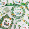 A set of green and white dinosaur-themed disposable tableware including plates, napkins, and a banner.