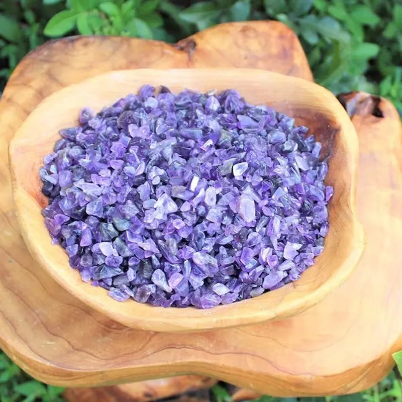 Purple tumbled gemstone chips in a wooden bowl resting on a natural wood surface.