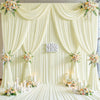 A luxurious cream fabric backdrop with draped curtains and floral accents for an event or wedding.