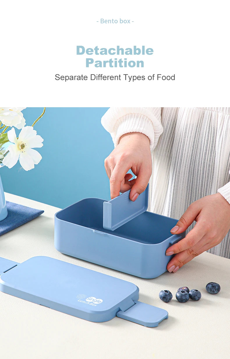 A light blue bento box is shown open on a white table, demonstrating its detachable partition feature.