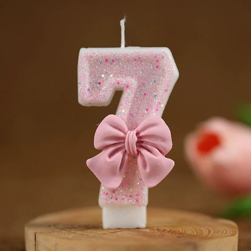 Vela número 7 de purpurina rosa con lazo sobre una superficie de madera.