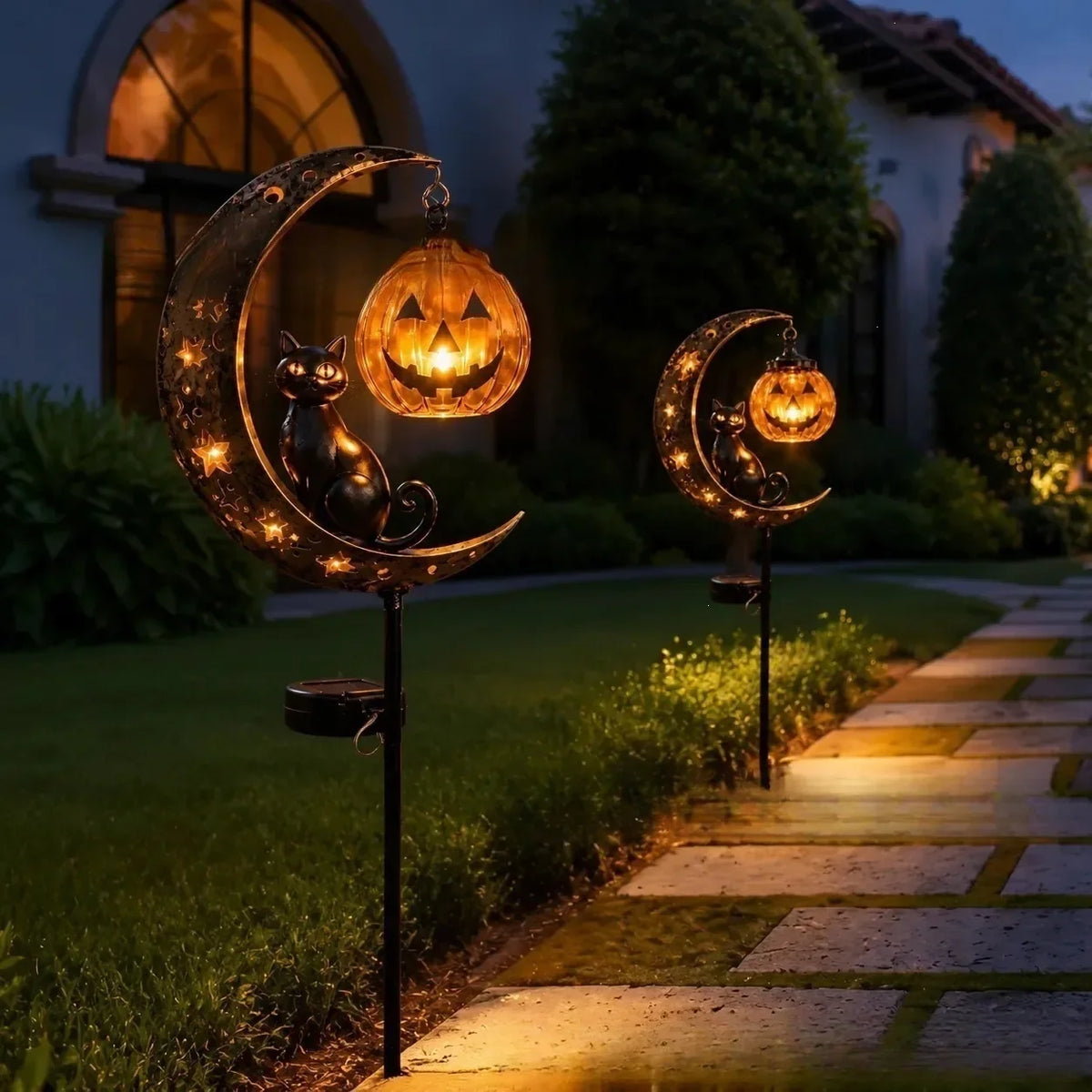 A solar Halloween lantern featuring a crescent moon and black cat silhouette illuminating a garden path at dusk.
