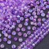 A close-up view of small, round purple AB crystal glass beads scattered on a dark surface.