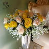 A bouquet of peach and yellow roses mixed with baby's breath flowers in a silver vase.