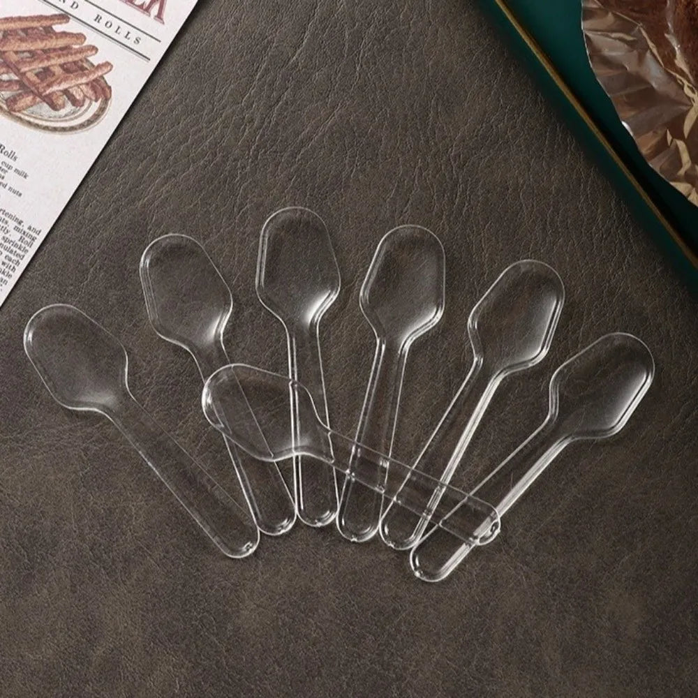 A collection of clear plastic disposable spoons arranged on a dark surface.