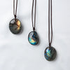 A dark, oval labradorite gemstone pendant on a brown leather cord.