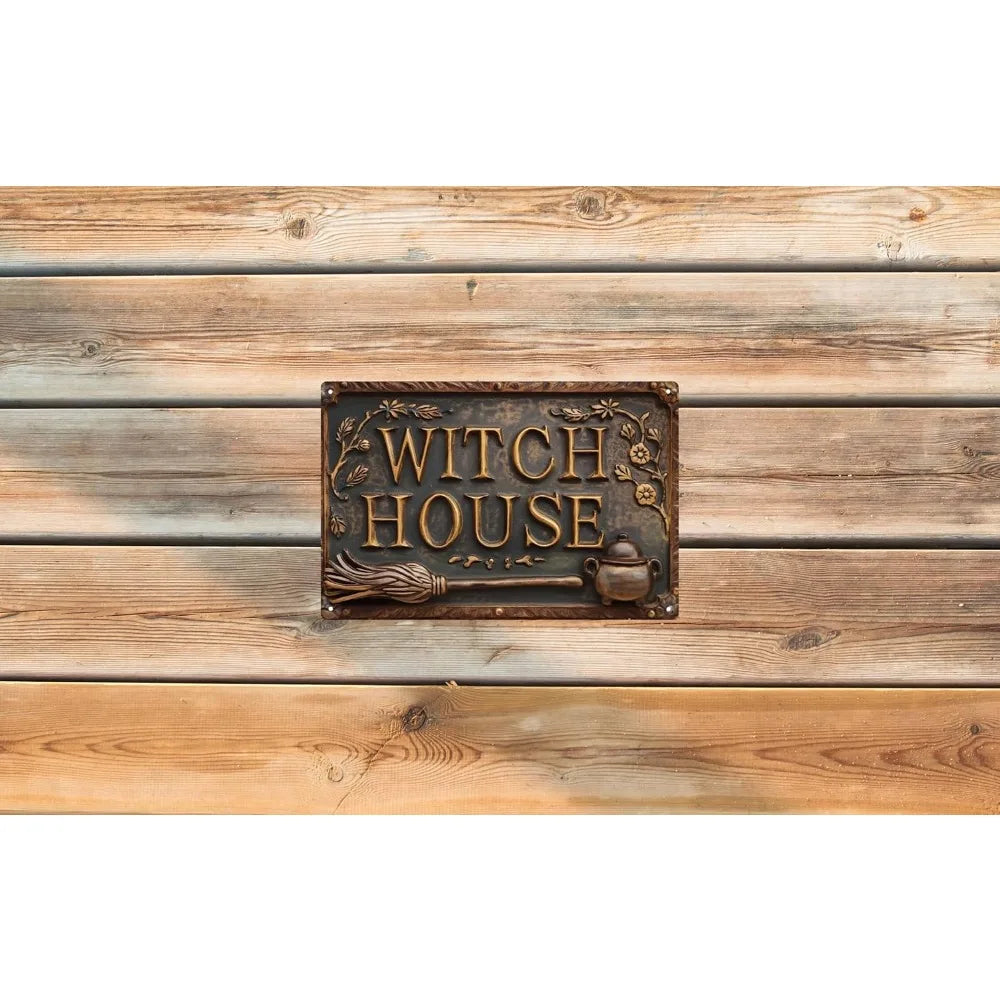 A vintage metal sign with the words WITCH HOUSE and a broom and cauldron design mounted on weathered wooden planks.