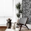 A dark gray chair sits next to a potted plant in a bright room with white blinds and black and white zebra print wallpaper.