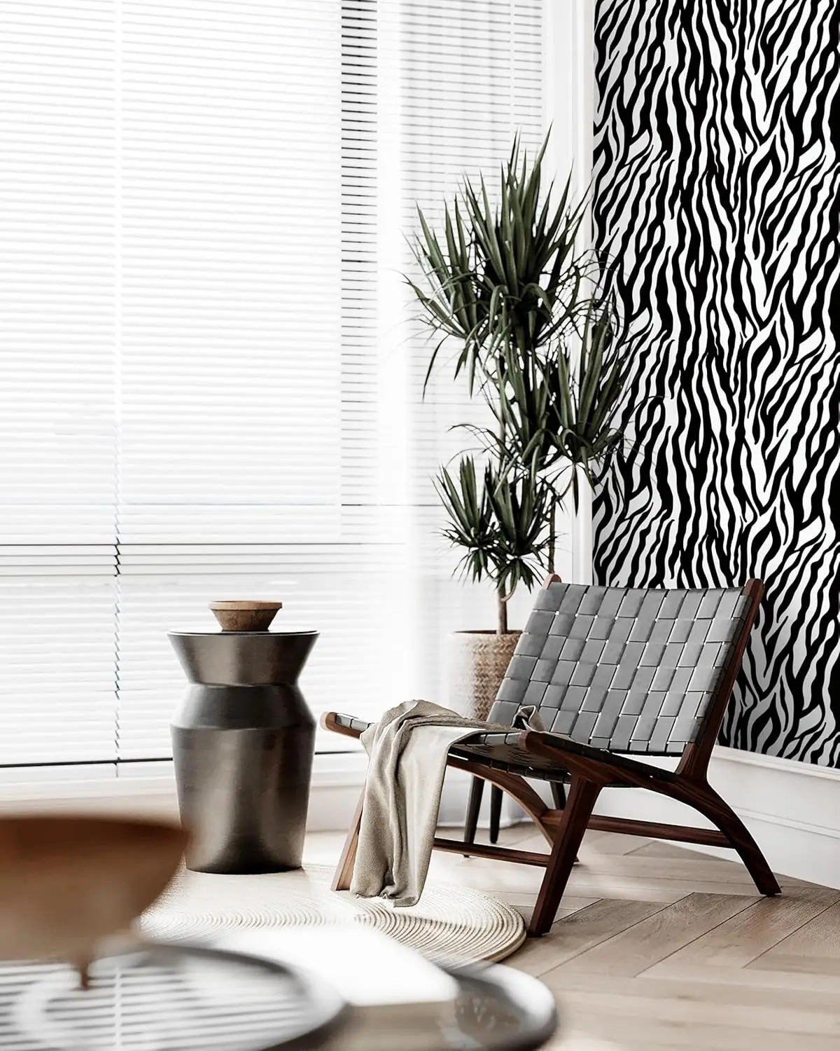 A dark gray chair sits next to a potted plant in a bright room with white blinds and black and white zebra print wallpaper.