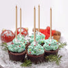 A set of metallic gold birthday cake candles with holders displayed on a white surface surrounded by green foliage.