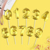 A collection of gold numbered candles, 0 through 9, on white sticks, against a yellow background.