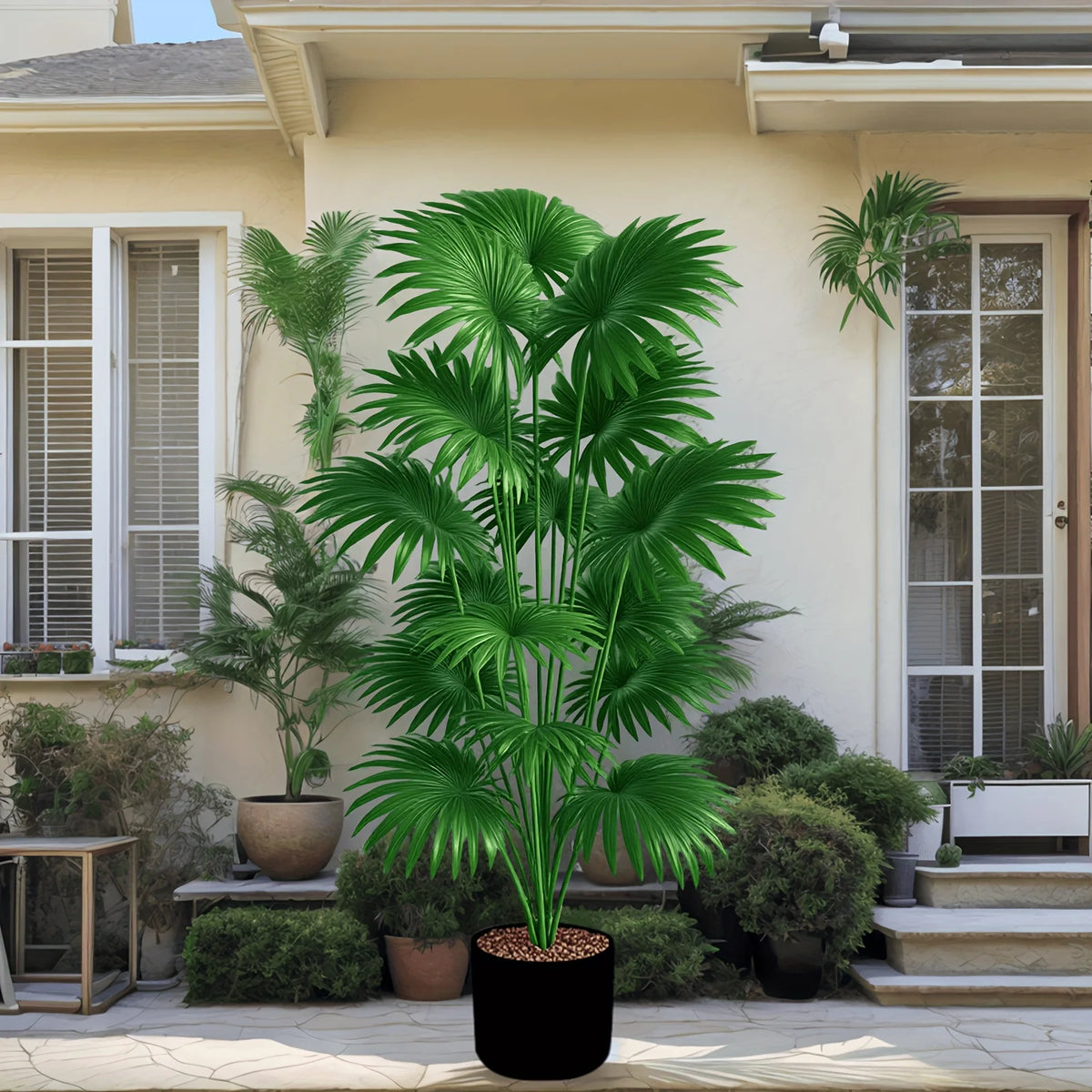 Large artificial palm tree in a black pot placed outdoors near a house entrance.