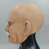 A realistic latex mask of an old man's head, showing wrinkled skin and an open mouth, displayed on a black mannequin.