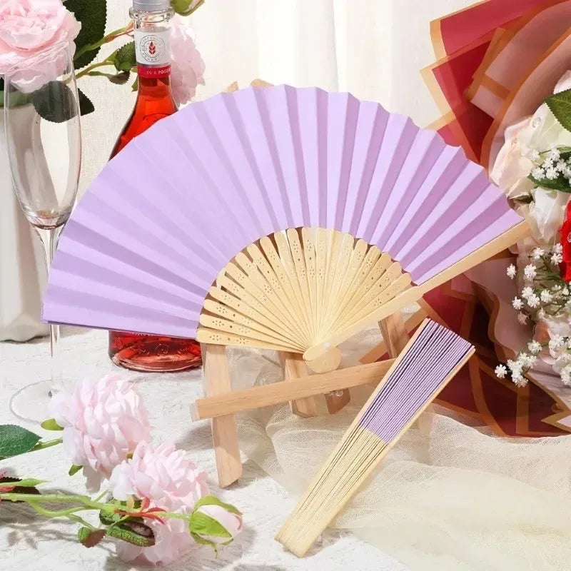 Élégantes éventails pliants à main pour femmes en lavande et rose avec des nœuds décoratifs, présentés sur un tissu blanc.