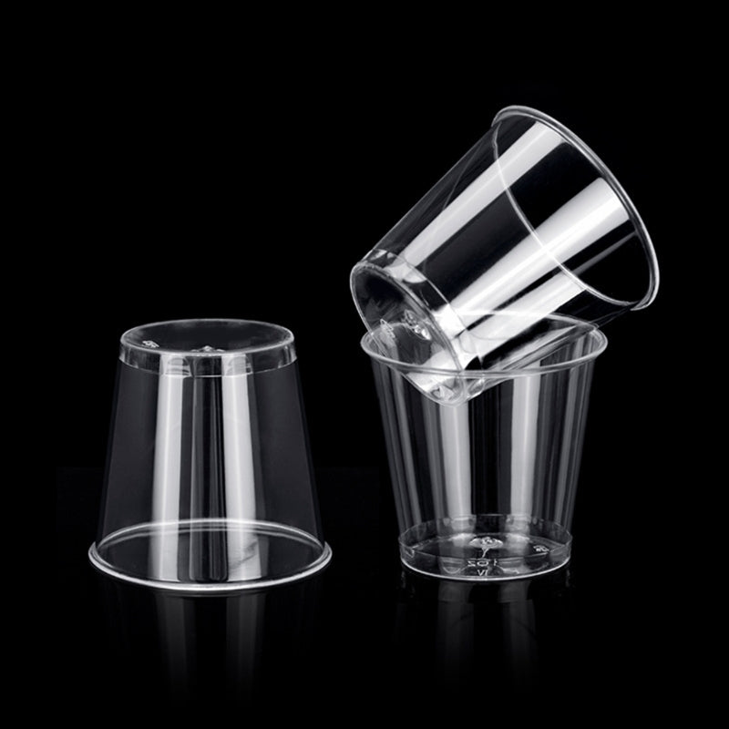 A clear plastic shot glass is shown tilted against a black background.