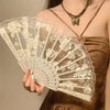 A hand holds an elegant white lace rose folding fan against a brown garment.