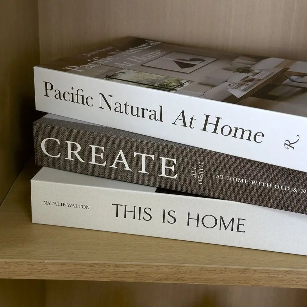 A display of three books titled Pacific Natural At Home Create and This Is Home on a wooden shelf.