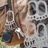 A collection of durable stainless steel keychains with multi-loop designs are displayed against a brown canvas bag.