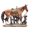 A sculpture of a brown horse with a saddle and bridle standing next to a wooden fence.