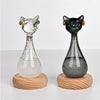 A glass bottle decoration shaped like an Egyptian cat, featuring a clear body and black details, resting on a wooden base.