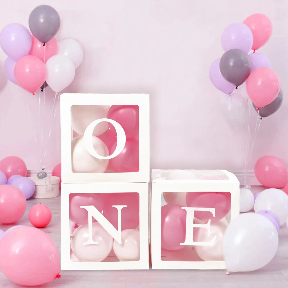 A white box with a cutout shaped like the letter O holds pink and white balloons for first birthday decorations.