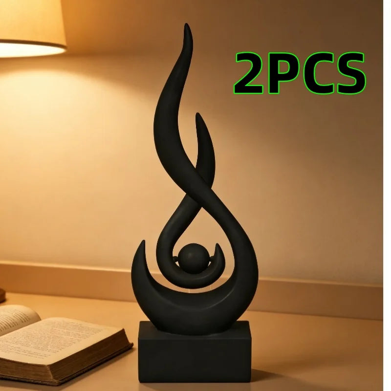 Two black flame sculptures on a dark base next to an open book.