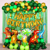 A balloon arch setup featuring foil balloons in green and gold, a tinsel curtain backdrop, and dinosaur-themed props.
