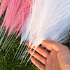 A hand holds a bundle of white and pink artificial reeds or pampas grass for home and event decor.