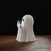 A white glow-in-the-dark ghost figurine with a playful pose sitting on a dark wooden surface.