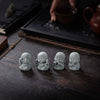 Four small grey stone monk statues for meditation and zen decor placed on a dark wooden surface.