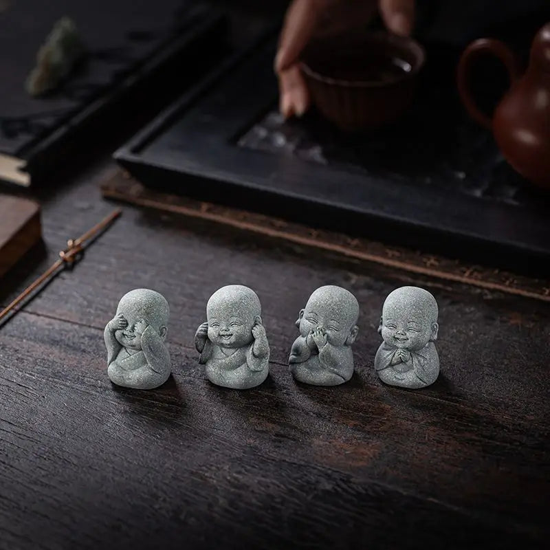 Four small grey stone monk statues for meditation and zen decor placed on a dark wooden surface.