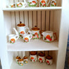 A display of handcrafted miniature mushroom tableware set for dollhouses on a white shelf.