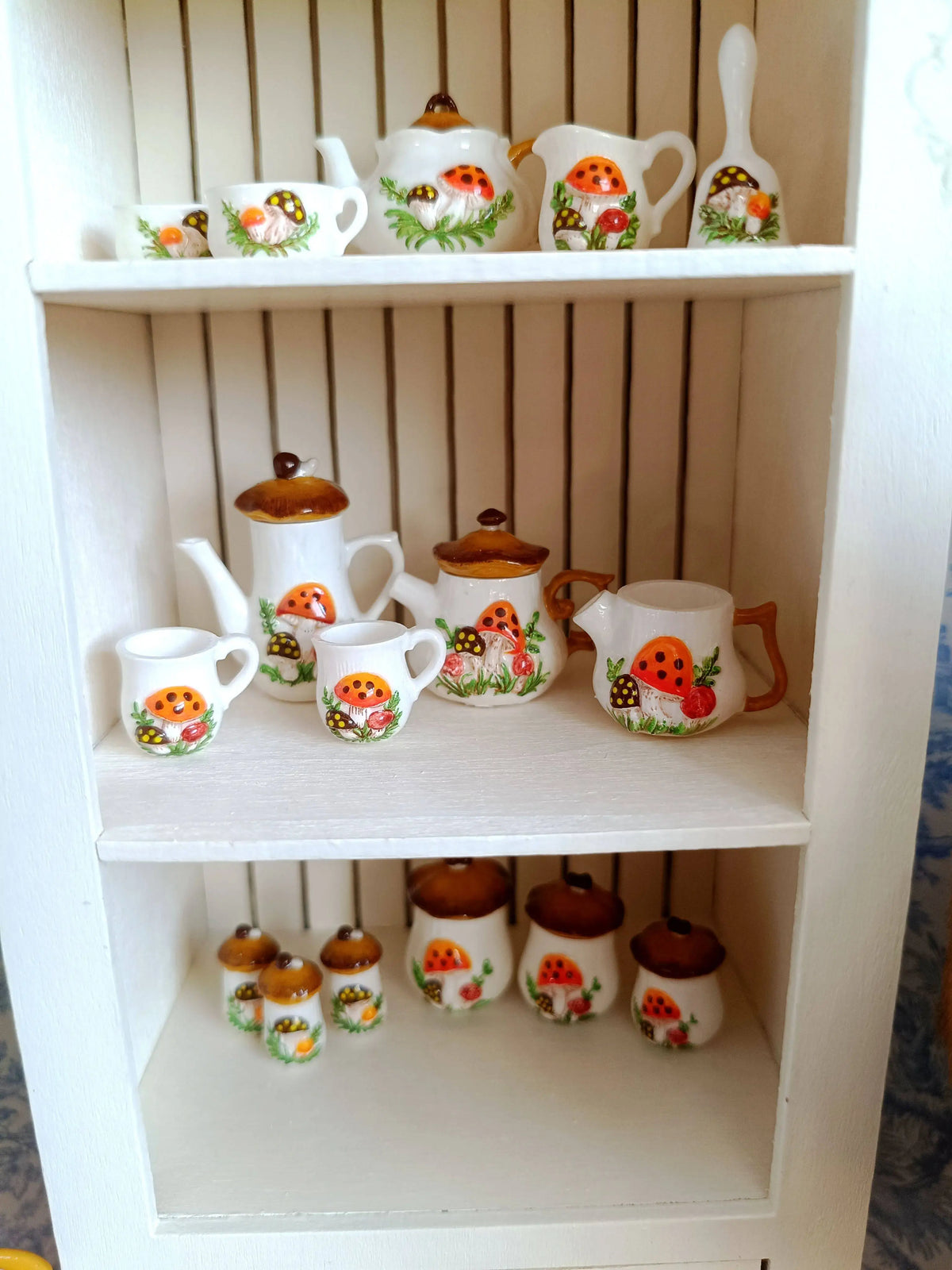 A display of handcrafted miniature mushroom tableware set for dollhouses on a white shelf.
