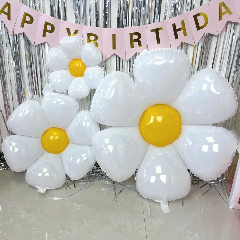 A bouquet of white and yellow foil balloons shaped like daisies is displayed against a silver backdrop.