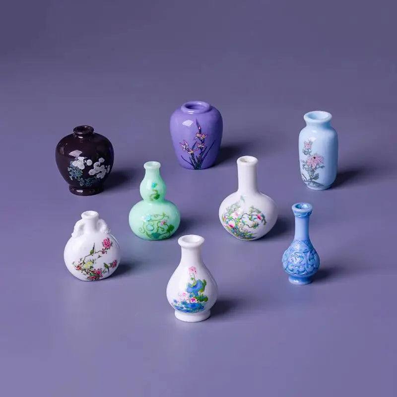 A collection of eight mini resin vases in various shades of purple and blue with floral patterns displayed on a gray surface.