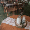 White embroidered lace table runner with dried greenery and candles on a wooden slice.