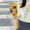 A graduation themed bouquet featuring a crocheted flower and a small teddy bear tied with a ribbon.